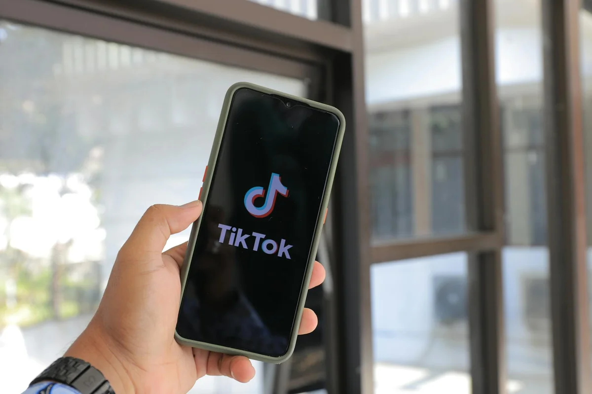 Formatos de contenido en TikTok: la guía del libro para eleg... — Close-up of a hand holding a smartphone displaying the TikTok app indoors.