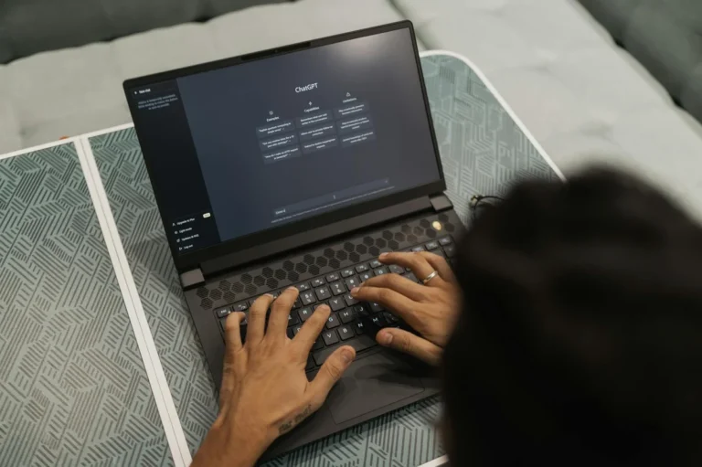 Cowork: cómo hacer que la IA mueva archivos y organice tu or... — Close-up of hands typing on a laptop displaying ChatGPT interface indoors.