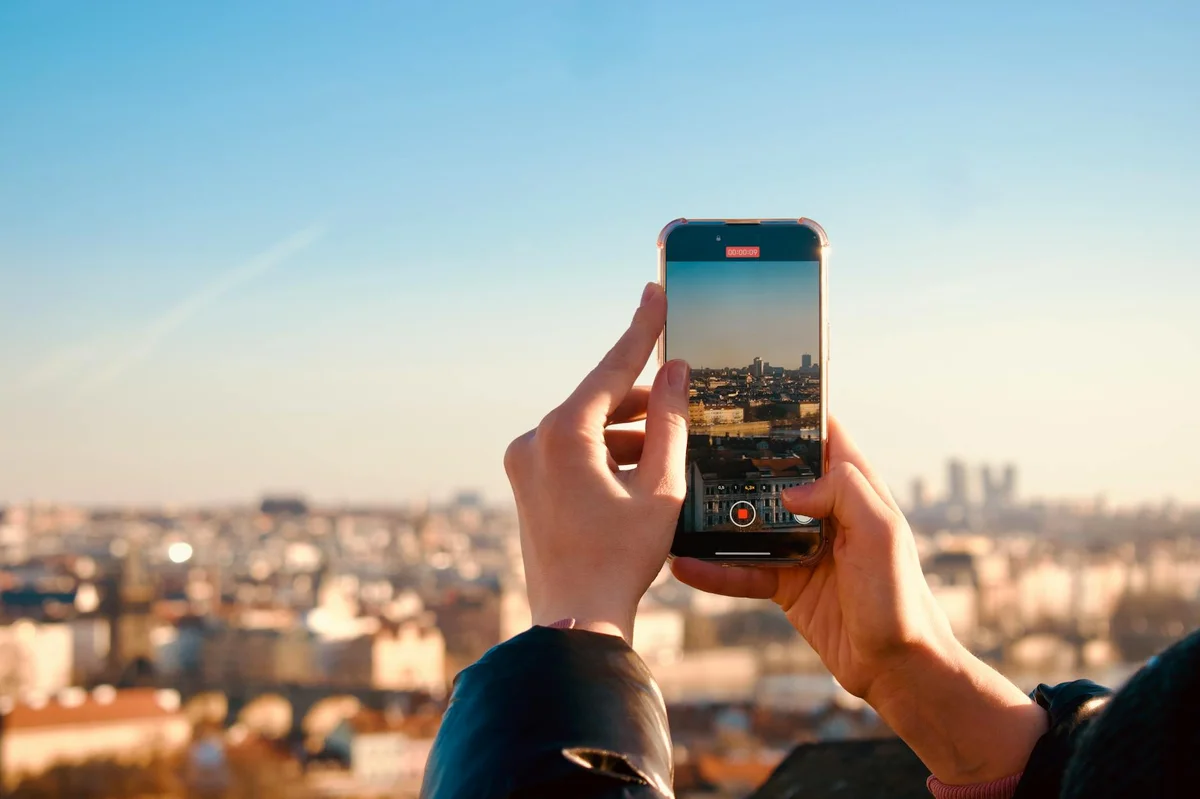 Psicología de la atención en TikTok: las claves del libro pa... — Hands holding a smartphone taking a photo of a city skyline during sunset, refle
