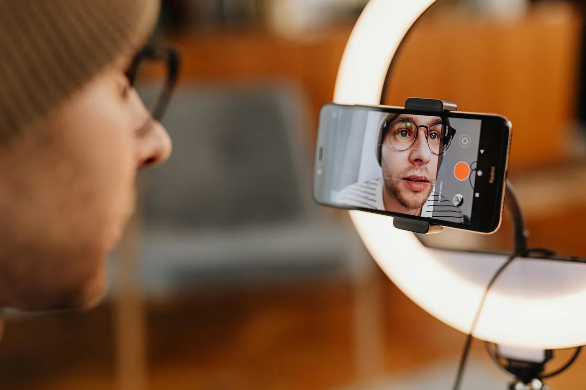 Analítica en TikTok: las métricas que el libro te enseña a l... — Close-up of a man recording a video with a smartphone and ring light indoors.