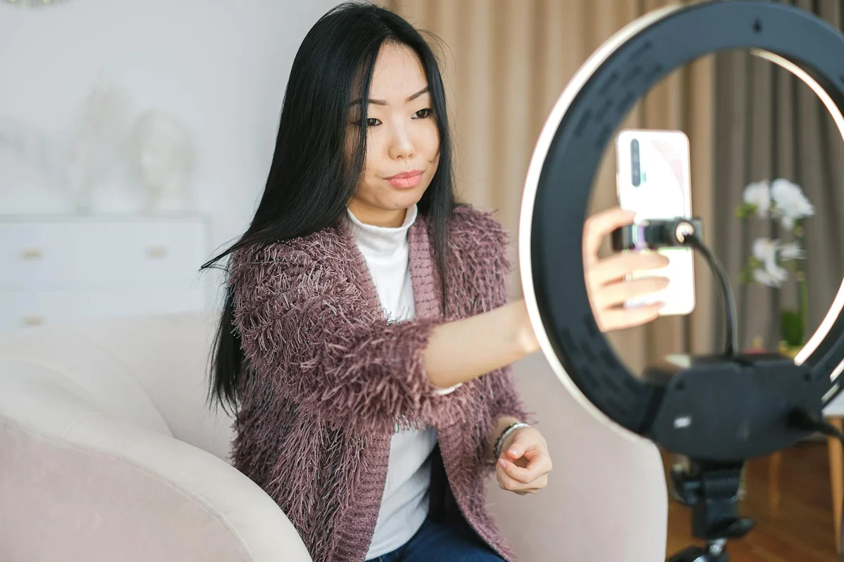 Ritmo de publicación y edición en TikTok: las claves del lib... — Asian woman using smartphone and ring light for vlogging indoors.