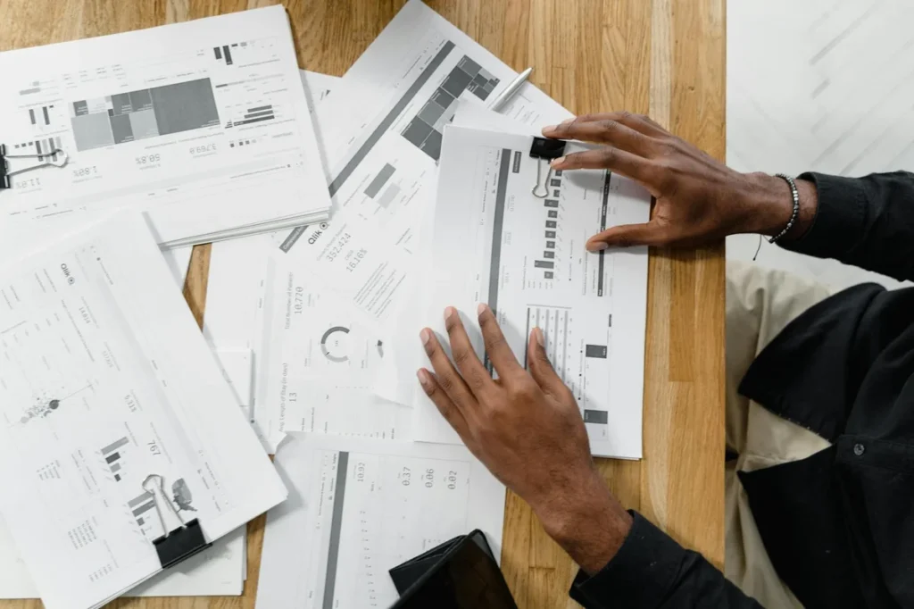 El arte de preguntar con IA: cinco niveles para descomponer... — Top view of a professional reviewing financial documents at a wooden workspace.
