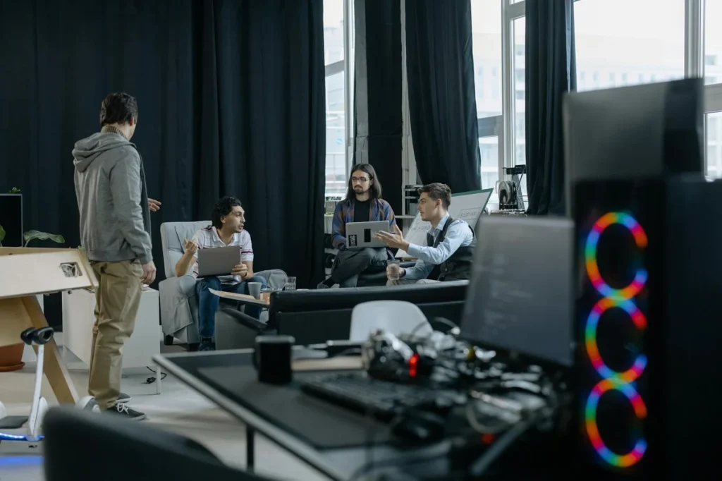 Proyectos largos con IA: el pase de testigo que mantiene la... — A group of professionals engaged in a casual meeting at a modern office, discuss