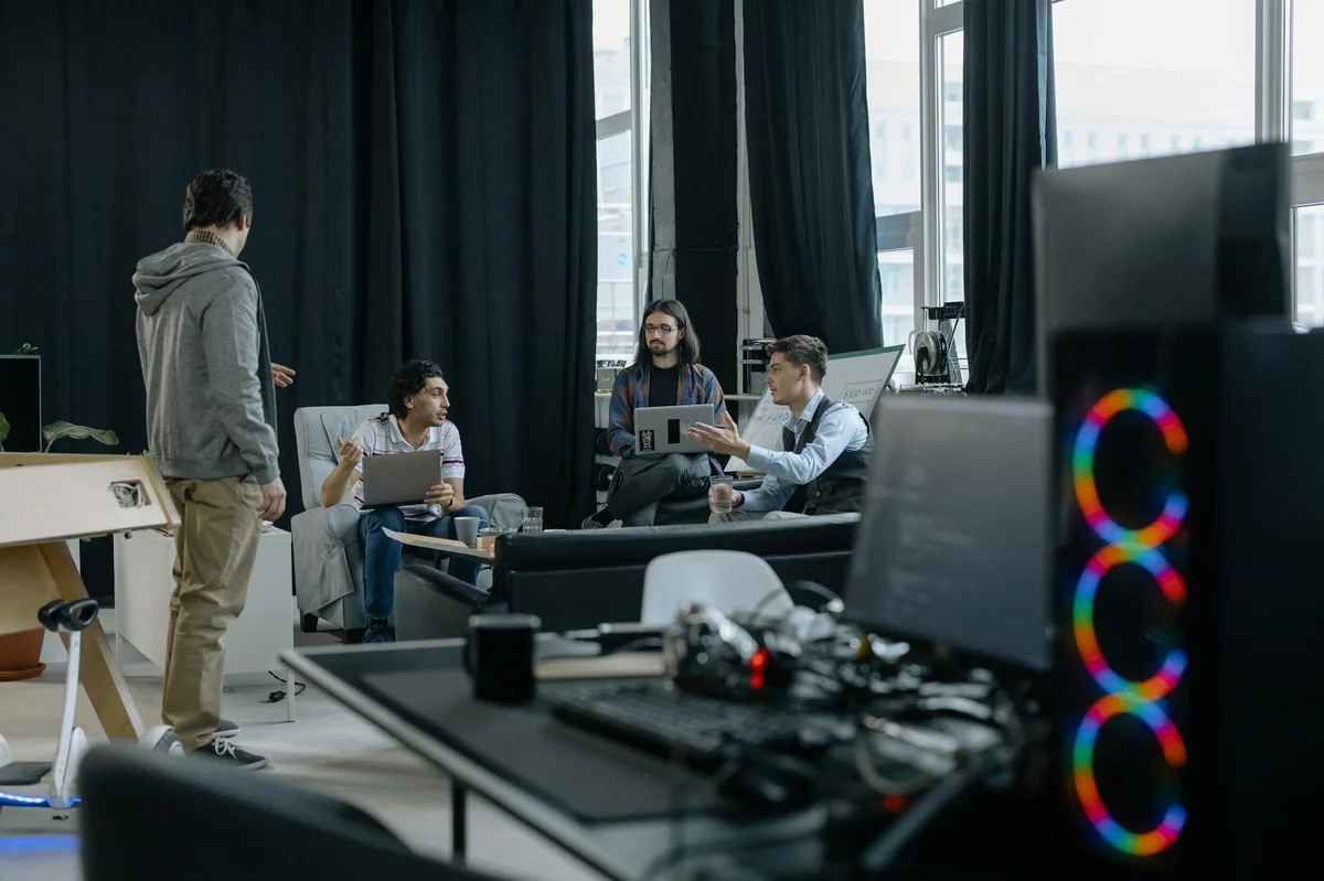 Proyectos largos con IA: el pase de testigo que mantiene la... — A group of professionals engaged in a casual meeting at a modern office, discuss