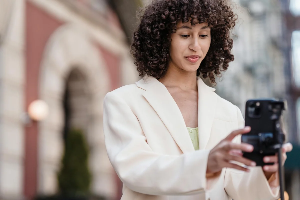 Tu perfil de TikTok como herramienta de conversión: lo que e... — Young ethnic female vlogger with curly hair in jacket preparing cellphone for vi