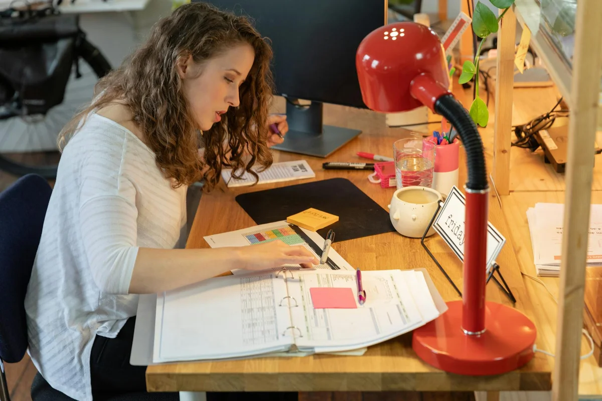 Como dejar de estar ocupado y empezar a ser eficaz: lo que e... — Woman working intently at her desk in a cozy office, surrounded by documents and