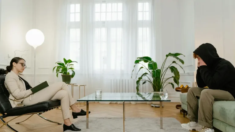 A therapist listens to a patient in a comfortable office setting. The atmosphere is calm and profess