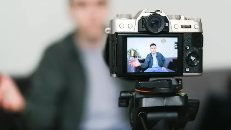 Man recording a vlog indoors using a mirrorless camera on a tripod with selective focus.