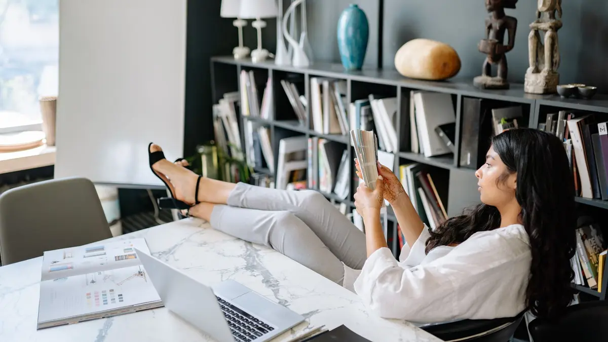 Woman reading a book in a modern office with laptop and papers, projecting a relaxing work environme