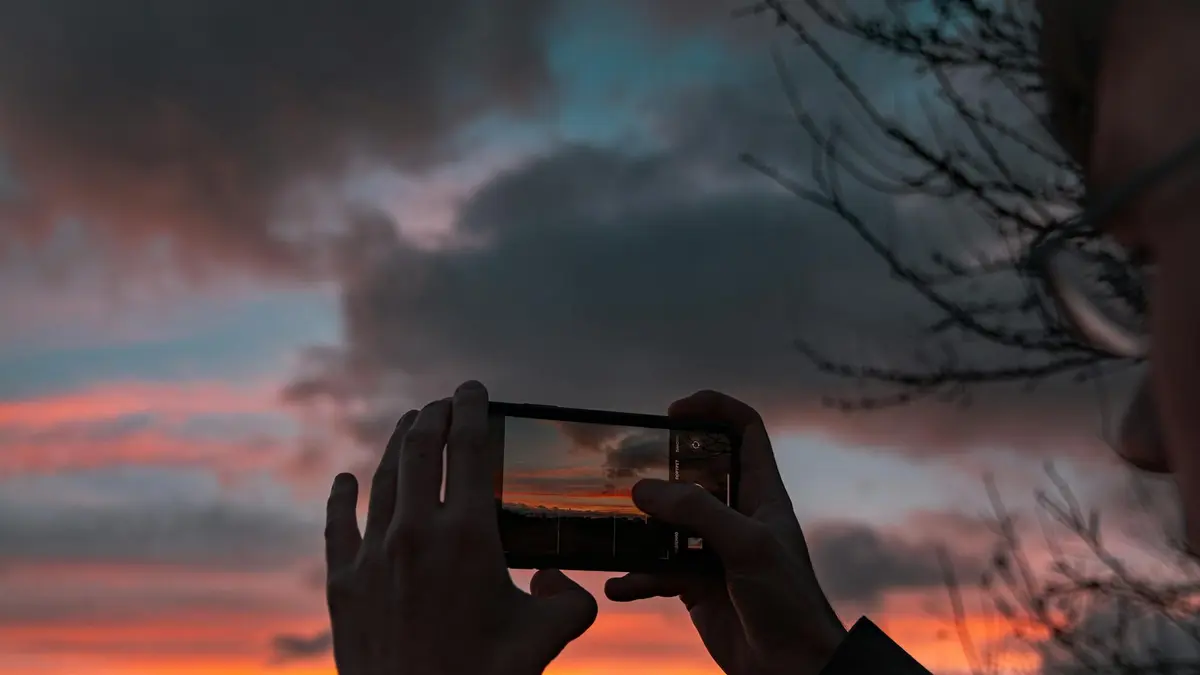 Silhouette of a person capturing a vibrant sunset with a smartphone in hand.