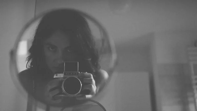 Moody black and white photo capturing a self-portrait in a round mirror, using an analog camera.