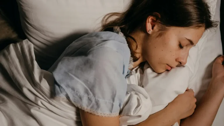 A serene young woman peacefully sleeping on a white pillow indoors at night.