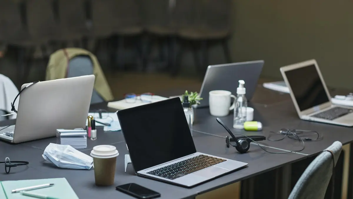 A cluttered office desk setup featuring multiple laptops, coffee cup, and office supplies for a busy