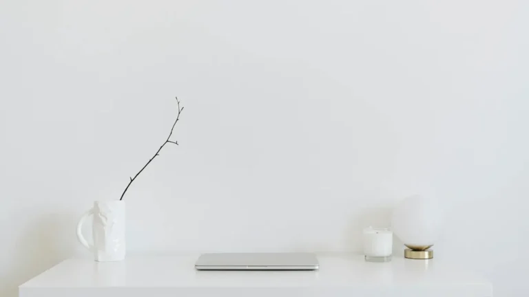 A clean, minimalistic workspace featuring a white desk, laptop, and decorative items, perfect for mo