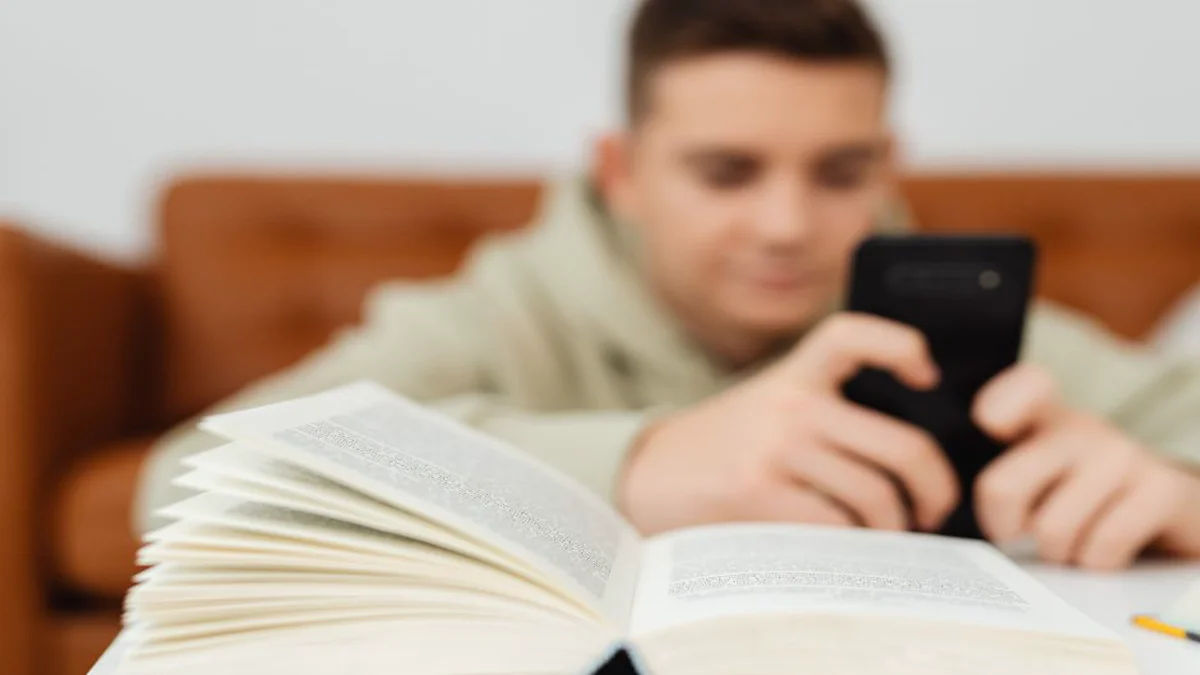 Hombre con smartphone junto a un libro abierto sobre la mesa